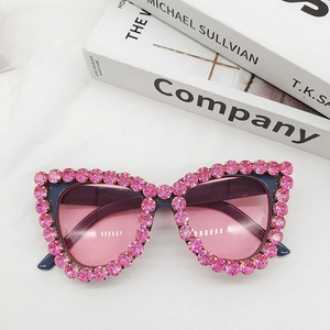 Detail of cat eye sunglasses with pink rhinestones and gradient lenses on books