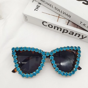 Close-up of cat-eye sunglasses with blue rhinestones on tortoise frame and dark lenses