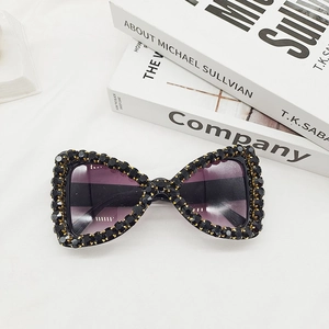Detail of butterfly-shaped sunglasses with black beaded frame and purple gradient lenses