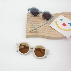 Flat lay of round frame kids sunglasses in sage green and cream on a wooden display