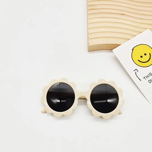 Detail der blumenförmigen Kinder-Sonnenbrille in Creme mit runden Gläsern auf Holzdeko