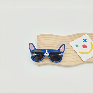 Blue dog-shaped children's polarized sunglasses with bulldog ears on a wooden tray