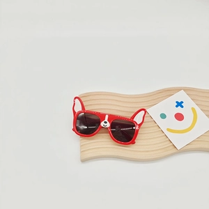 Detail of red cartoon dog sunglasses for kids with cute ear decor on a wooden display