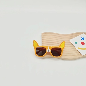 Detail view of orange cartoon dog-shaped kids sunglasses on a textured display stand