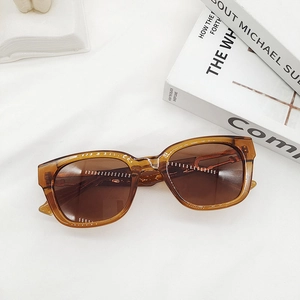 Gros plan de lunettes de soleil carrées marron translucide sur un fond de tissu blanc
