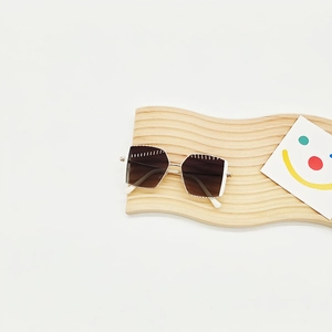 Detailansicht der quadratischen Kinder-Sonnenbrille mit braunem Farbverlauf auf Holz