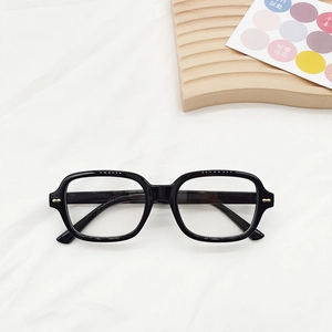 Gros plan sur une monture de lunettes carrée noire avec détails dorés sur bois