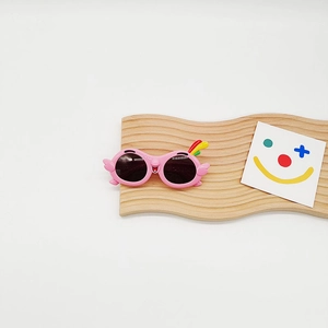 Detail of pink cartoon kids sunglasses with colorful parrot wings and crest on a wooden stand