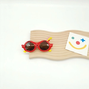 Detail of red cartoon bird sunglasses for kids on a wooden tray with a smiley card