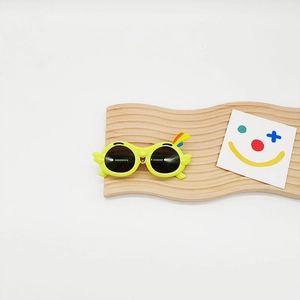 Detail of yellow parrot cartoon kids sunglasses with cute face on wavy wooden display