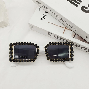 Detail of white rectangle sunglasses featuring black rhinestone trim on white fabric