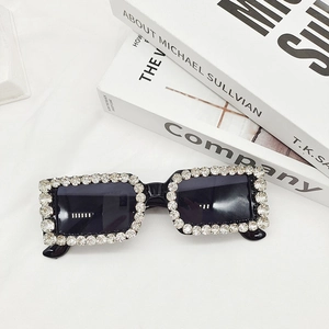 Close-up of rectangular black sunglasses with rhinestone-encrusted frames on white fabric