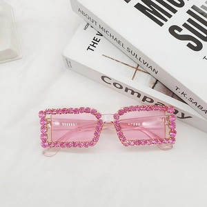 Detail of pink crystal-encrusted square sunglasses with retro Y2K aesthetic on white fabric