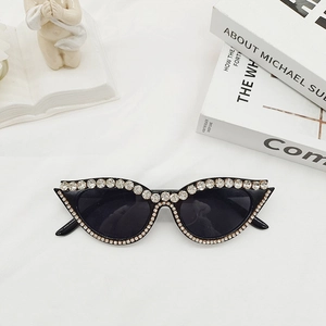 Détail de lunettes de soleil œil-de-chat noires avec cristaux de luxe sur tissu blanc