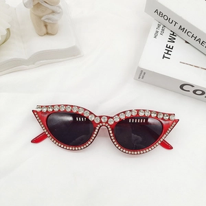 Gros plan de lunettes de soleil œil-de-chat rouges avec monture en strass sur tissu blanc