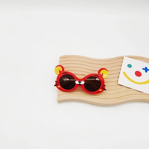 Vue détaillée des lunettes de soleil cartoon rouges pour enfants sur support bois