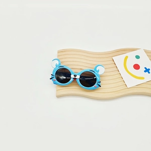 Détail de lunettes de soleil bleues en forme de souris posées sur un plateau en bois