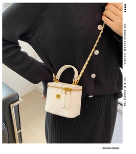 Detail view of white quilted vanity bag with golden camellia badge and chain strap