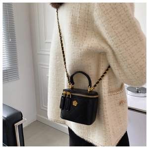 Detalle de bolso cubo negro acolchado con logo de camelia dorada y correa de cadena