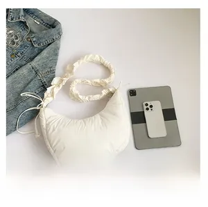 White puffy crescent moon bag shown next to a tablet and phone for size comparison