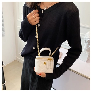 Detailed view of mini white quilted box bag with gold chain strap and petal metal accessory