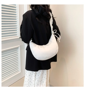 Close-up of white quilted crescent bag showing ruffled strap and bow detail on model