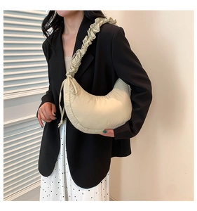 Detail of cream crescent shoulder bag with pleated strap worn with a black blazer