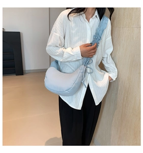 Detail of light blue crescent bag featuring pleated shoulder straps and quilted texture