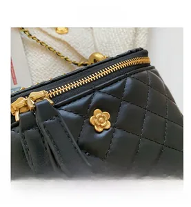Detail of black quilted leather bucket bag with gold flower logo and metal zipper
