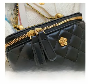 Close-up of golden camellia metal charm and dual zipper on quilted leather vanity bag