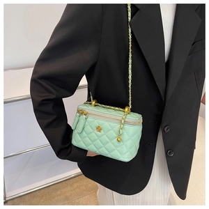 Detail of mint green quilted box bag with gold chain strap and floral emblem