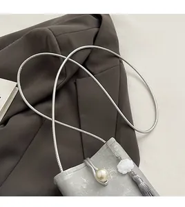 Détail du sac en soie argentée avec breloque lotus, perle et pompon en soie élégant