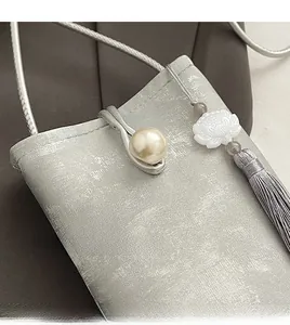 Détail du sac argenté avec fermoir perle, pendentif fleur de lotus et pompon gris