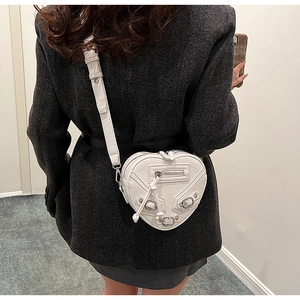 Détail du sac bandoulière blanc en forme de cœur avec rivets et boucles de style moto