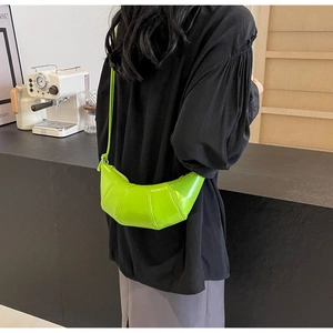 Detail of bright green croissant bag with glossy pleated texture and adjustable strap