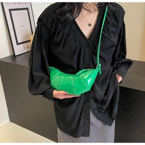 Close-up of a green crescent horn bag with pleated leather texture worn by a model