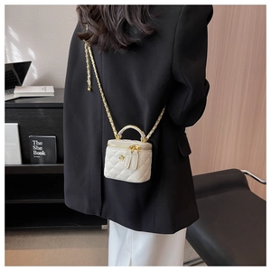 White quilted vanity case bag featuring a curved gold handle and chain strap on a model