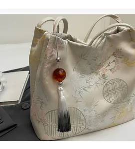 Dettaglio del ricamo floreale e nappa d'ambra sulla borsa a secchiello in jacquard