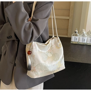 Dettaglio di ricami floreali e nappe su una borsa a secchiello in raso beige da donna