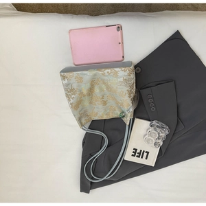 Dettaglio della borsa a secchiello jacquard azzurra con motivi dorati e nappe eleganti