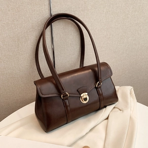 Elegante dunkelbraune Leder-Unterarmtasche mit Goldverschluss vor strukturierter Wand