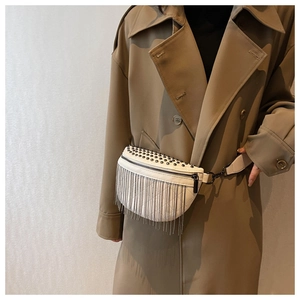 Detail of white saddle bag with silver metal rivets and long chain fringe on beige coat