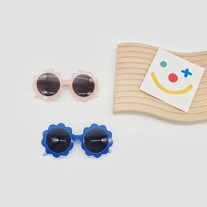Kids flower-shaped sunglasses in pink and blue for UV protection with wood tray