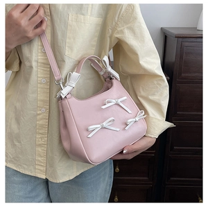 Pink saddle bag with white bow accents shown being worn by a model in a home setting