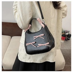 Detail of a black leather handbag with pink bows on a beige textured blazer jacket