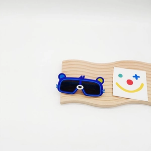 Lunettes de soleil bleues pour enfants avec oreilles d'ours sur un support en bois ondulé