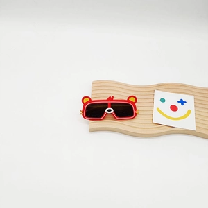 Détail de lunettes de soleil ours rouge pour enfants sur un support en bois naturel