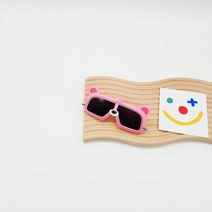 Détail de lunettes de soleil ours roses avec verres gris sur présentoir en bois ondulé