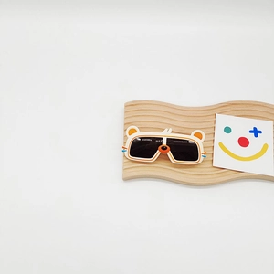 Détail de lunettes de soleil enfant beiges en forme d'ours sur un support en bois déco