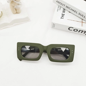 Detail of matte dark green rectangular sunglasses with silver rivets on a minimalist prop